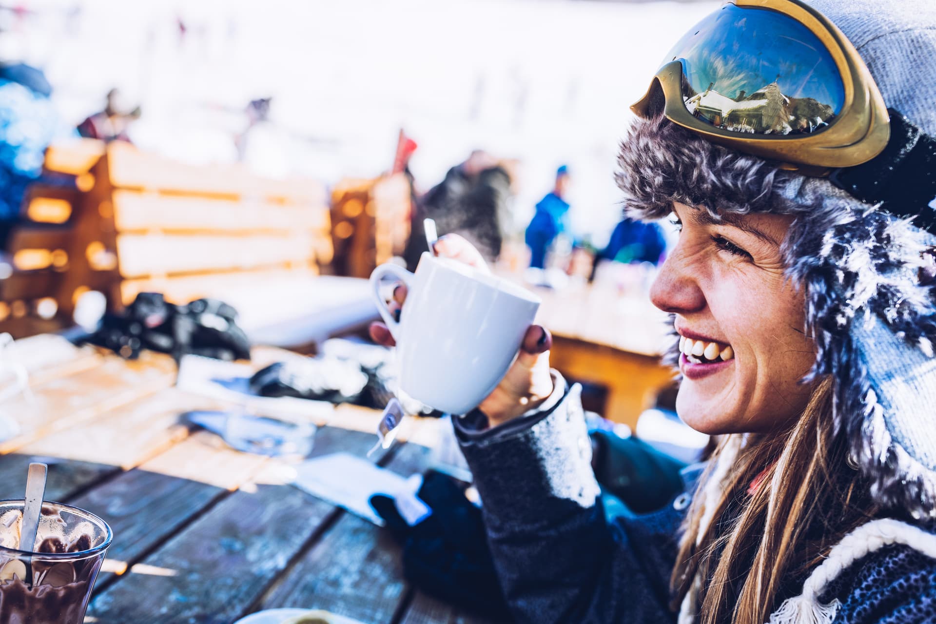 Woman wearing fluffy hat holding a cup of tea and smiling across the table