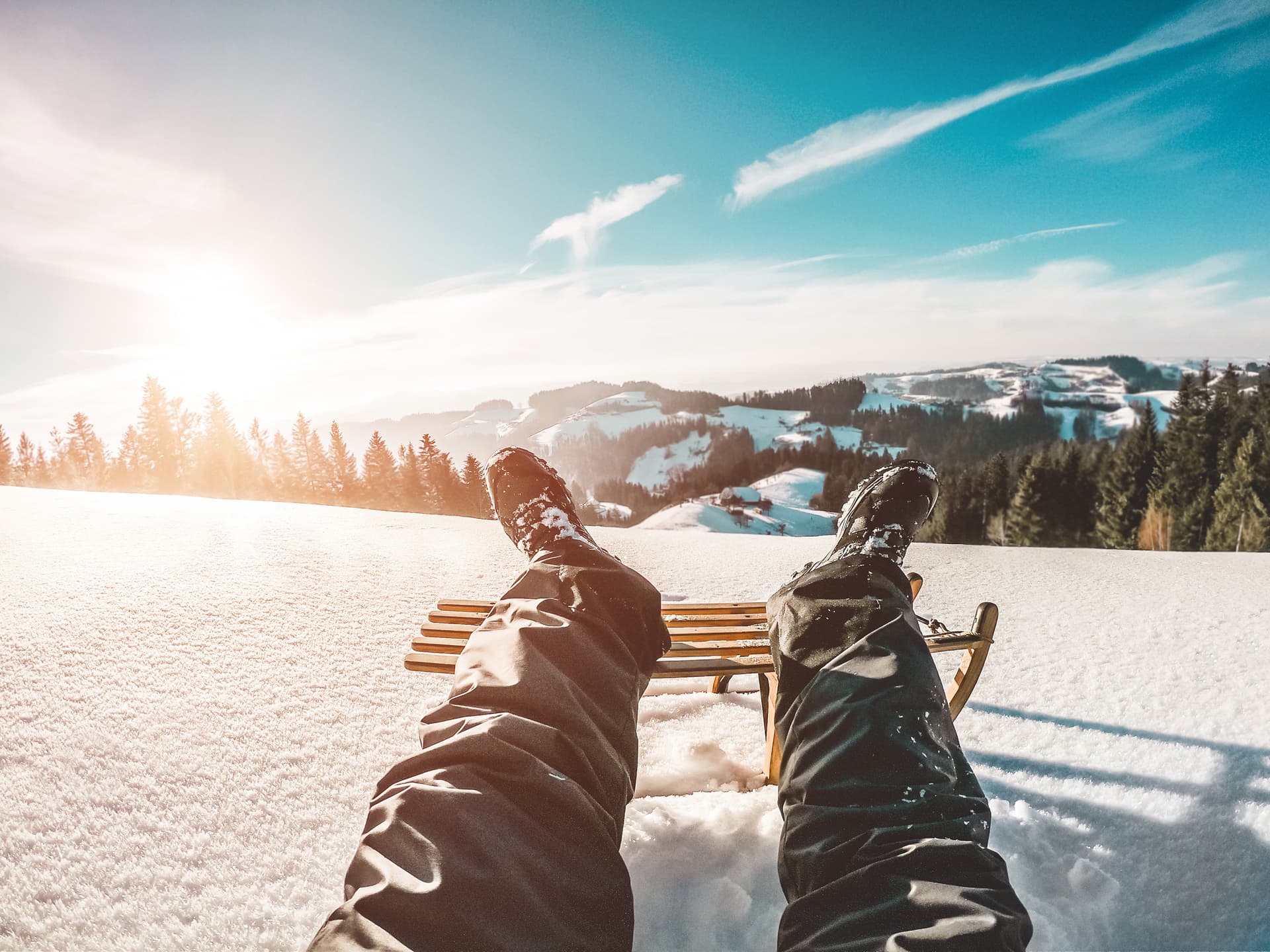 Feet resting on sledge with snow and trees in the background
