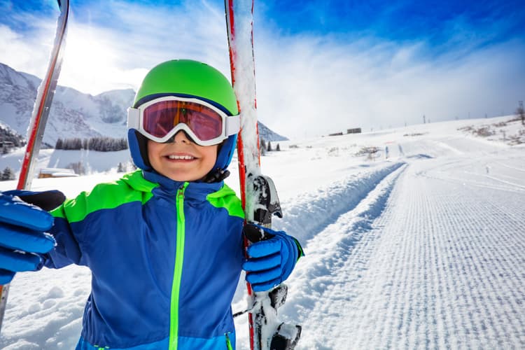 smiling happy child holding skis on mountain ski slopes
