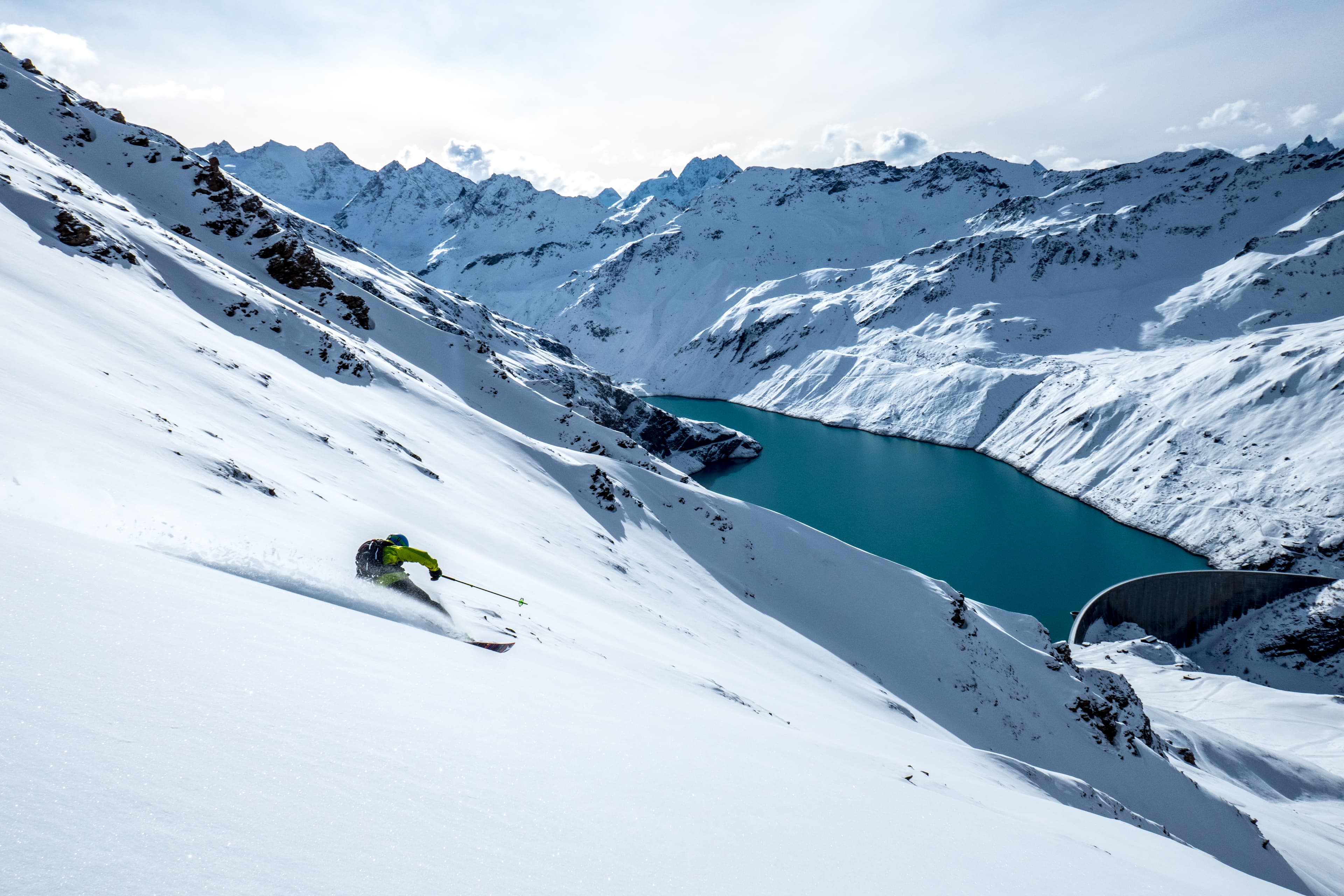 Skiier skiing down off piste slope with lake in background