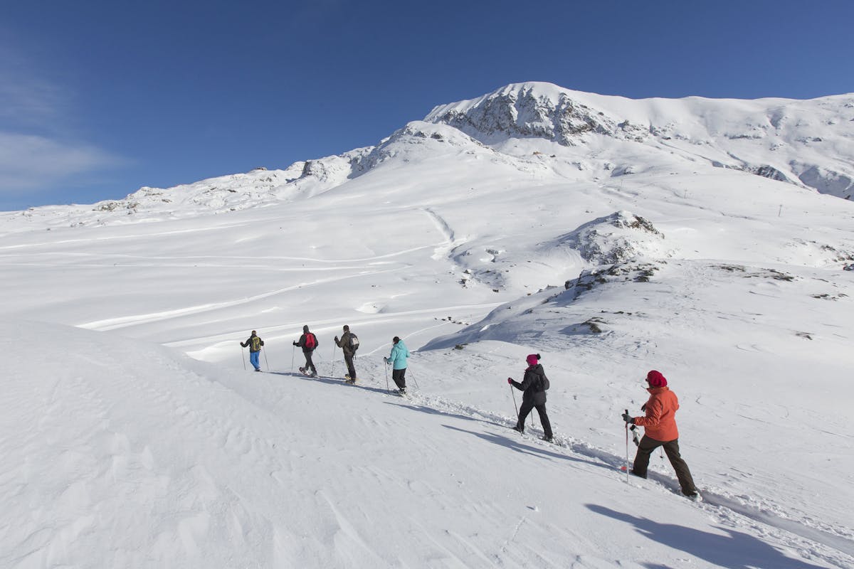 Group of people snowshoeing across snowy plain in French Alps resort Alpe D'huez