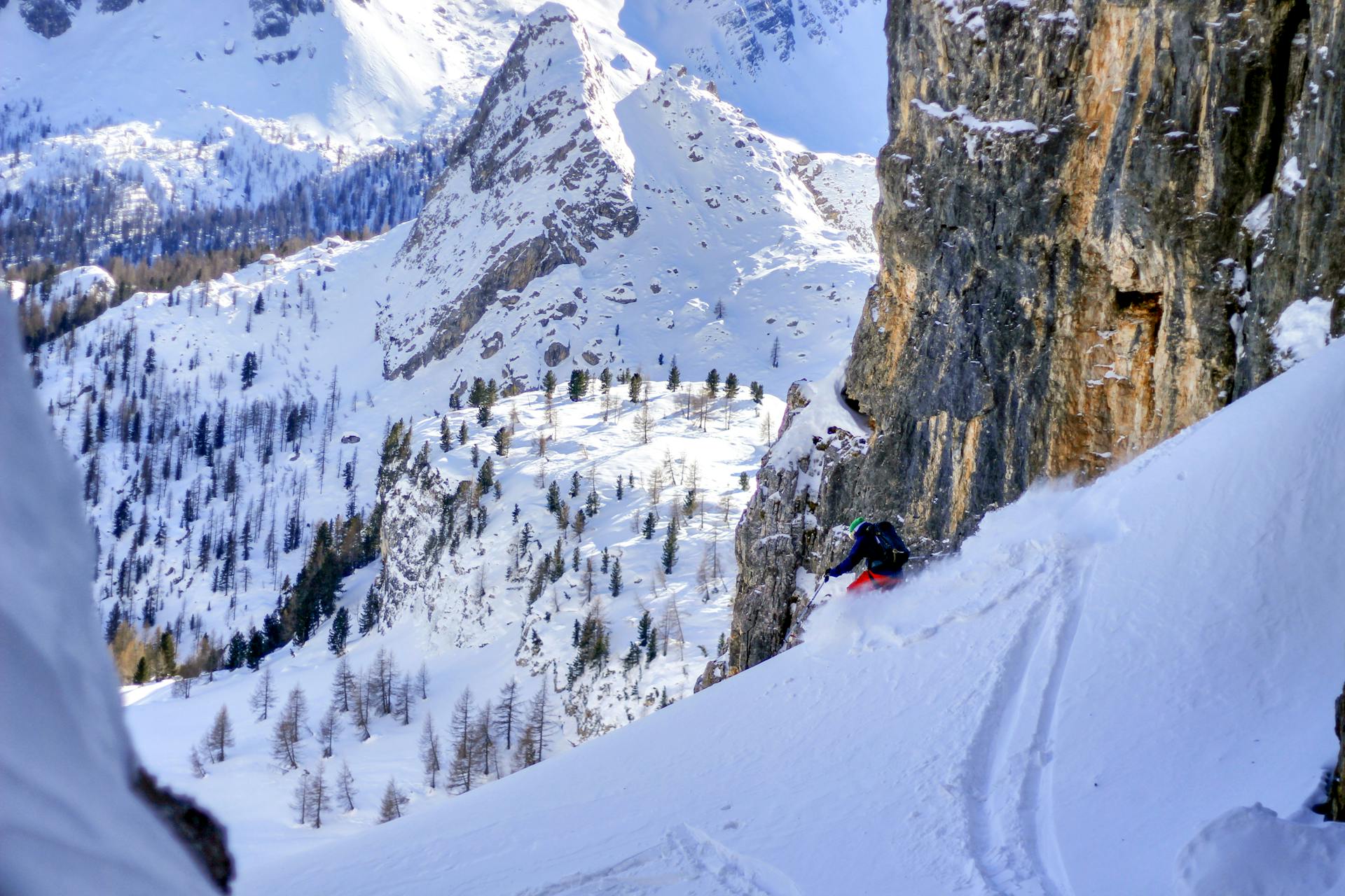 Skiier skiin down off piste slope between rocky mountain faces