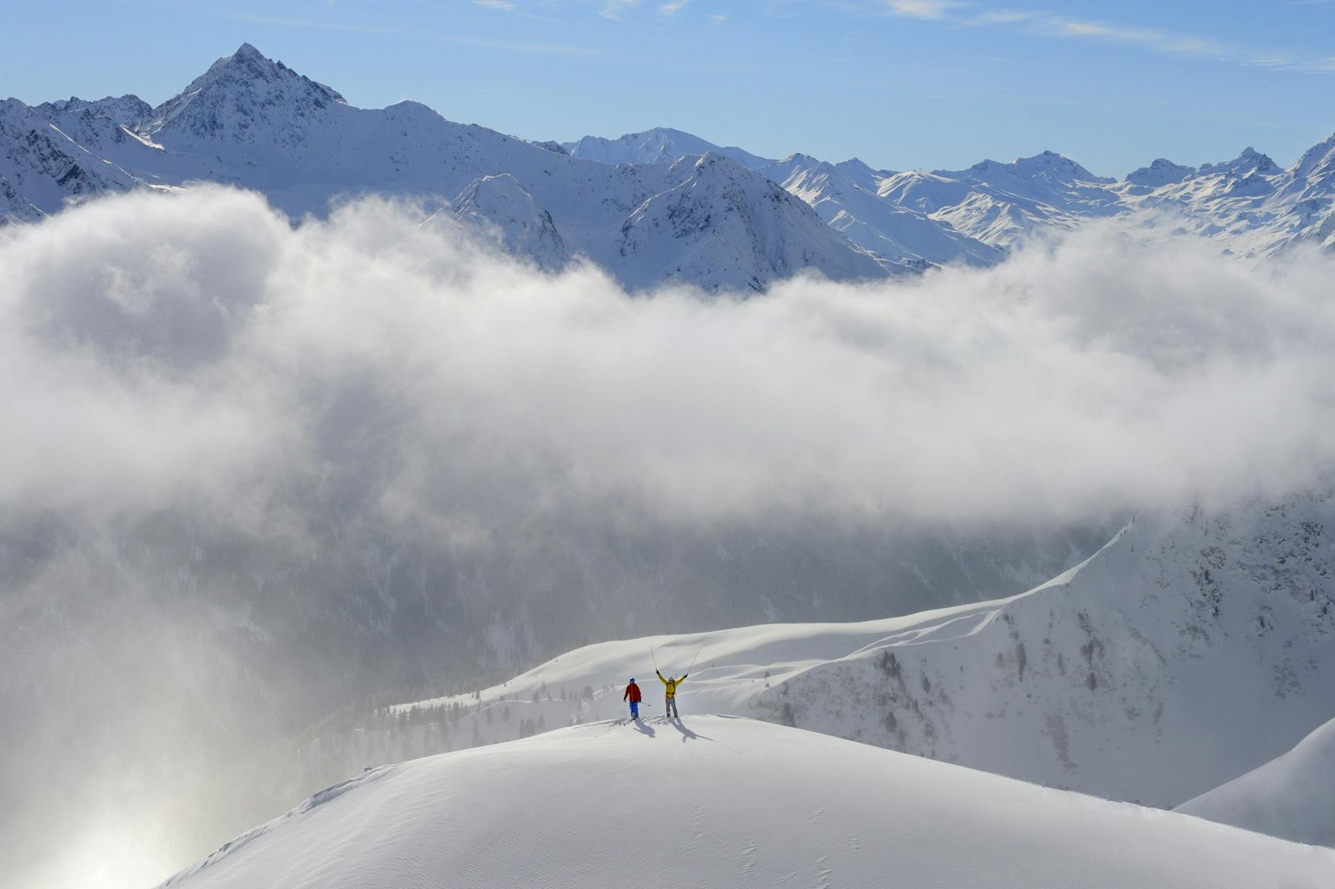 2 skiiers at peak of mountain with arms in the air