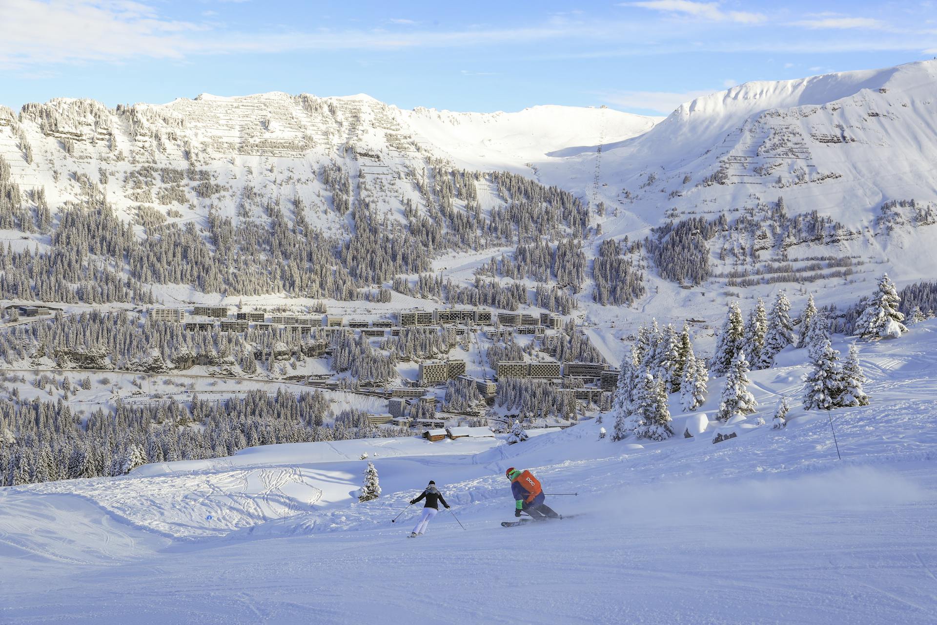 Skiiers skiing down slope into Flaine ski resort on bluebird day