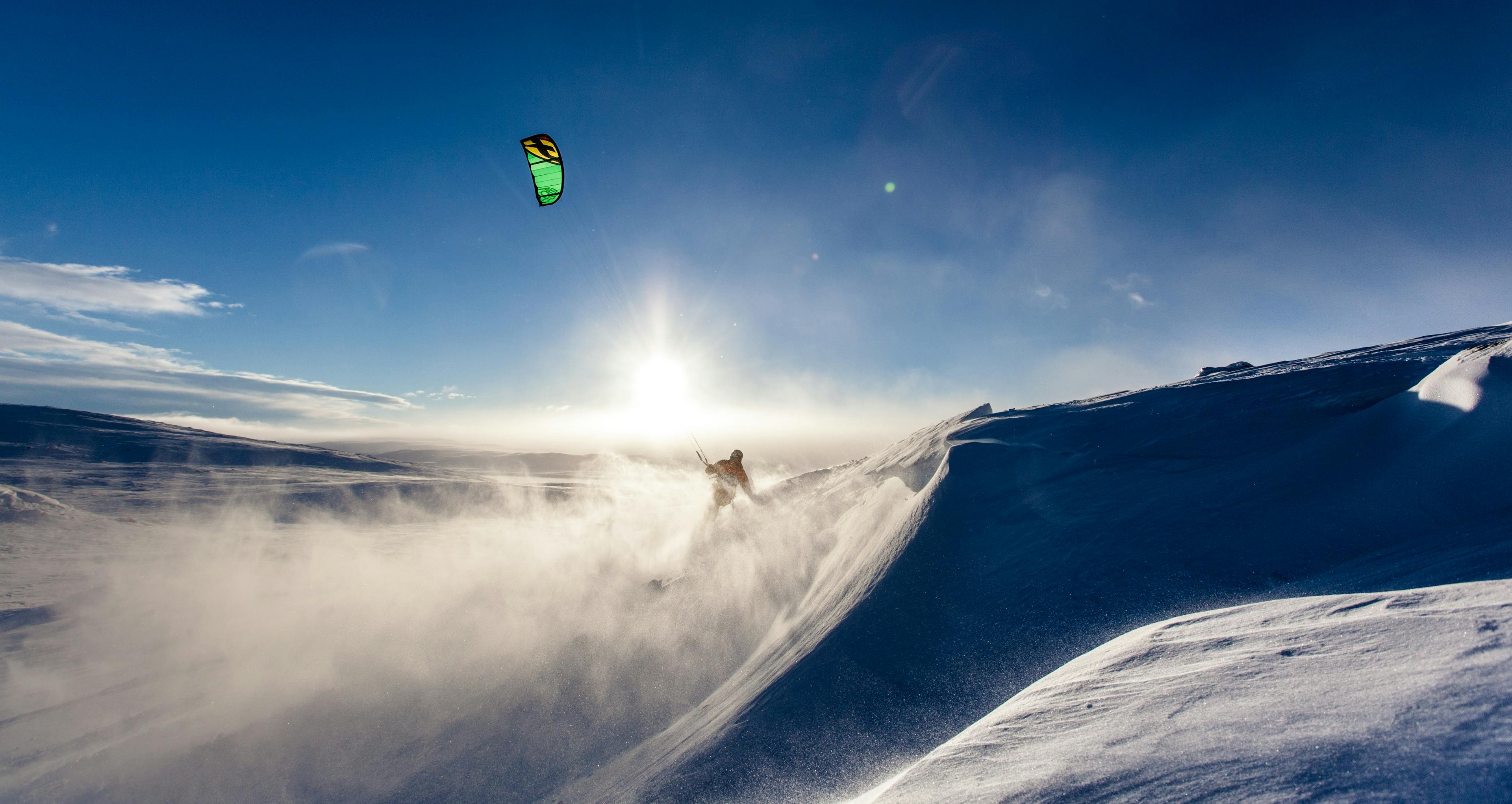 Man snow kiting on snowy mountain on holiday at sunset