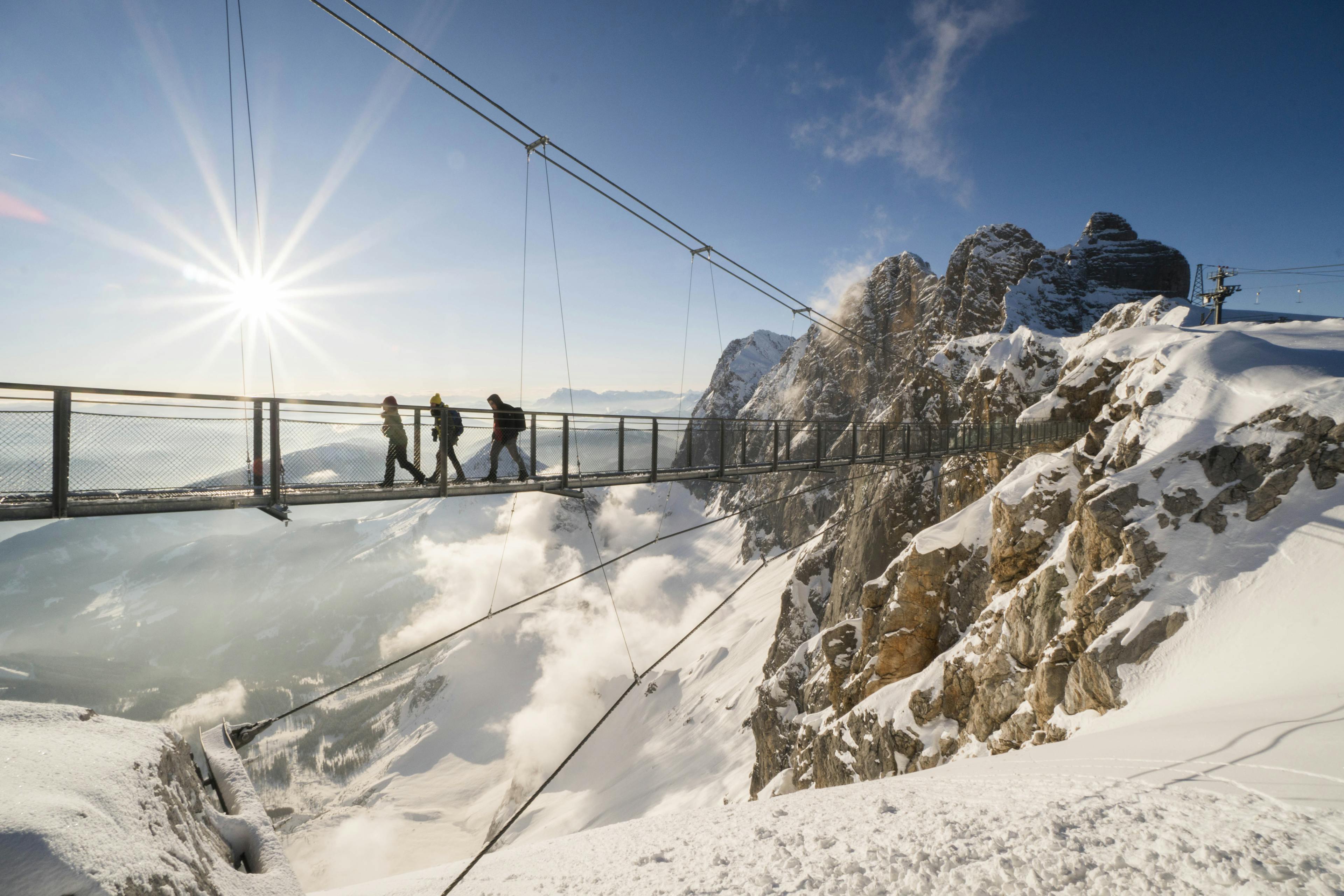 Walkers crossing bridge at high altitude in snowy mountains of schladming ski resort