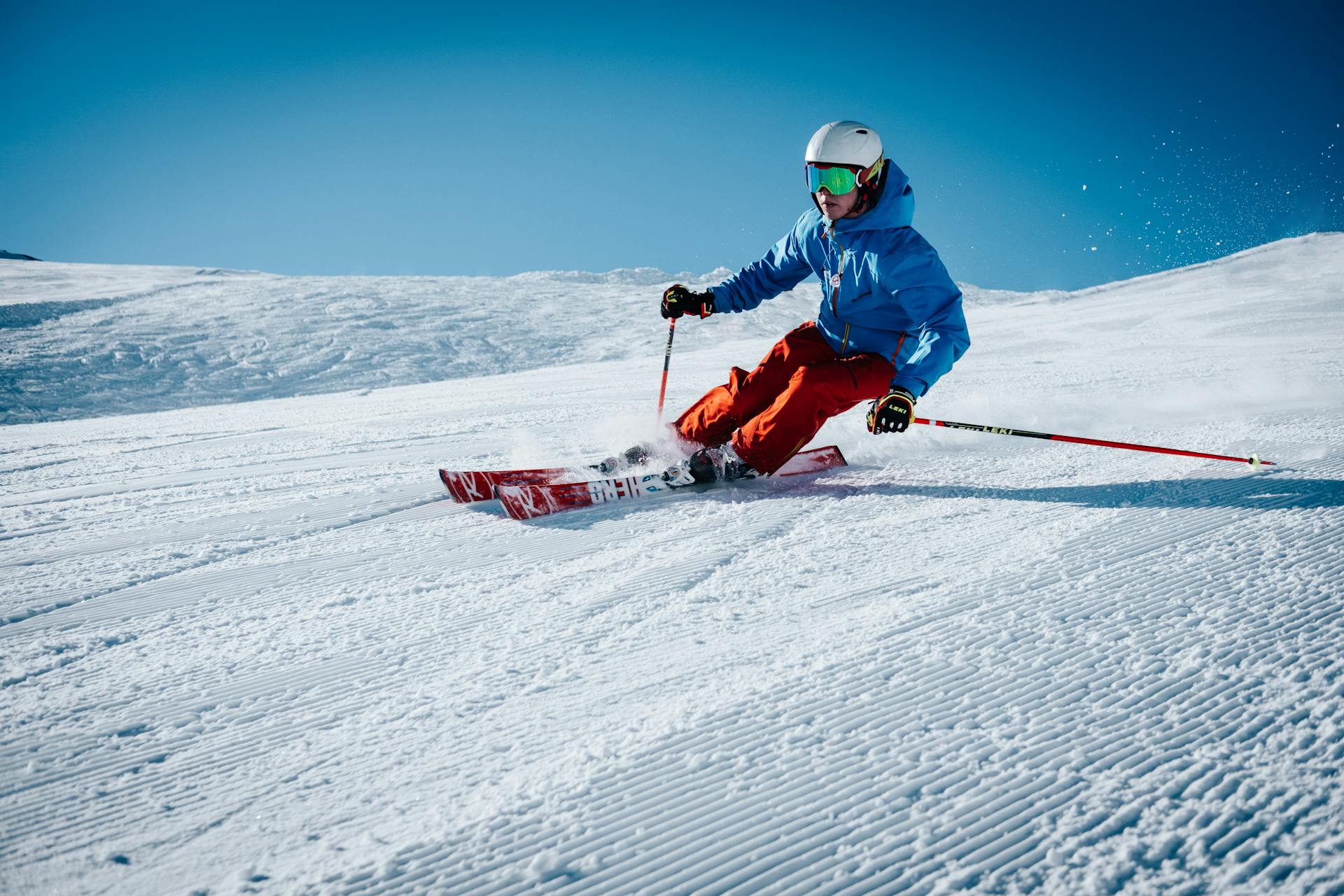 Skier in blue jacket and red trousers skiing down quiet wide slope