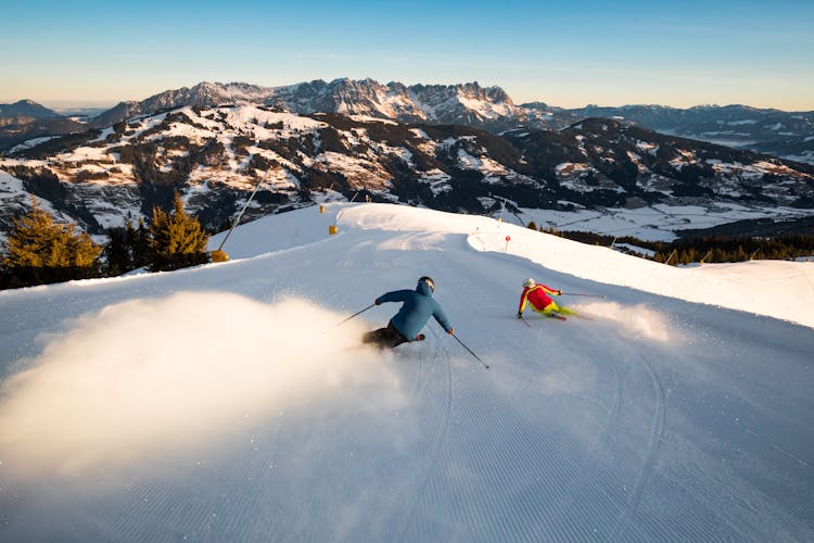 Two skiers carving down slope in Austrian ski resort of Brixen Im Thale