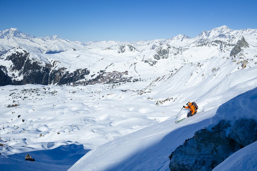 Skiier in orange jacket skis down off-piste slope in French alps